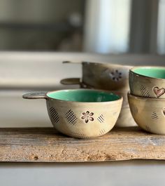 three metal bowls sitting on top of a wooden table with hearts painted on the lids