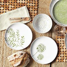 four plates with designs on them are sitting on a place mat next to bread and utensils