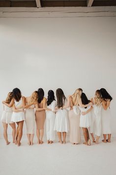 a group of women in white dresses standing next to each other with their arms around one another