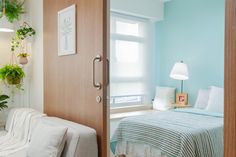 a bed sitting next to a wooden door in a bedroom under a window with potted plants on the wall