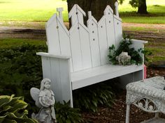 a white bench sitting under a tree next to a garden area with statues on it