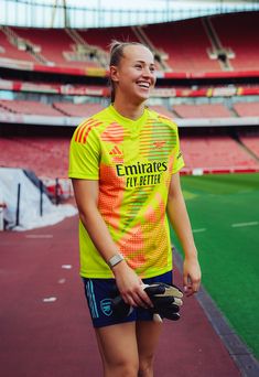 a woman standing in front of a soccer field wearing a yellow shirt and blue shorts