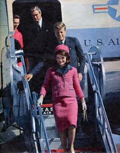 a woman in a pink suit and hat walking up stairs to an airplane with two men standing behind her