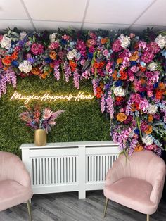 two pink chairs sitting in front of a green wall with flowers and words on it