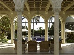 an outdoor covered patio with wicker chairs and umbrellas in the shade, surrounded by palm trees