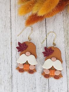 a pair of brown and white earrings sitting on top of a wooden table next to an orange feather