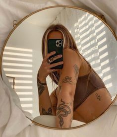 a woman with tattoos taking a selfie in front of a round mirror while holding her cell phone