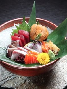 a bowl filled with sushi and vegetables on top of a wooden table next to a stone slab