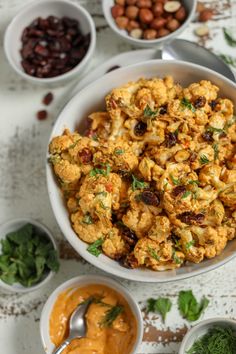 a bowl filled with cauliflower next to bowls of sauce and nuts on a table