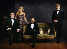 three people and a dog sitting on a couch in front of a black wall with a dark background