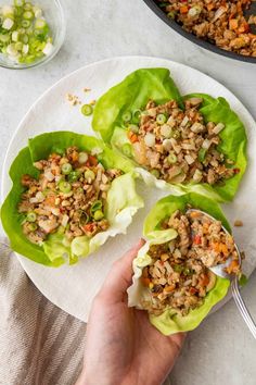 two lettuce wraps filled with meat and vegetables on a plate next to a skillet