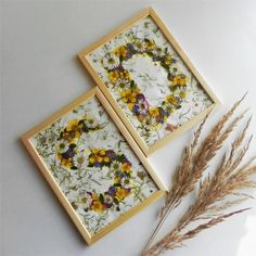 two framed pictures sitting next to each other on top of a white table with dried flowers