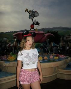 a woman standing in front of a mickey mouse statue with her hands on her hips