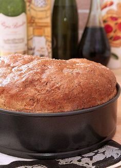 a loaf of bread sitting on top of a cake pan next to bottles of wine