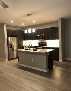 an empty kitchen and living room with wood flooring, stainless steel appliances and dark cabinets