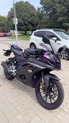 a black motorcycle parked in a parking lot next to a white car and some trees