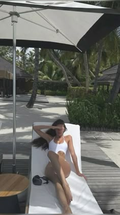 a woman sitting on top of a white towel next to a table with chairs and umbrellas