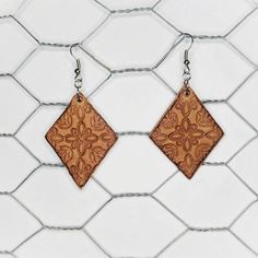 two square wooden earrings hanging on a chain link fence with white tiles in the background