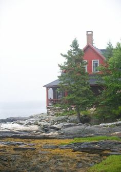 a red house sitting on top of a rocky shore