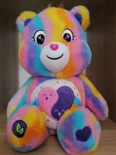 a rainbow colored teddy bear sitting on top of a wooden shelf