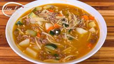 a close up of a bowl of soup with meat and vegetables on a wooden table