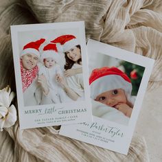 two christmas cards with santa hats on them sitting on a bed next to a flower