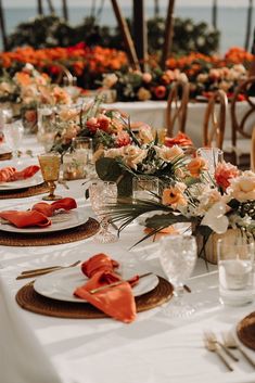 the table is set with orange and white flowers in vases, napkins, and place settings