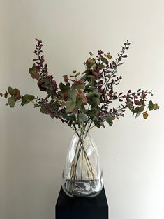 a vase with flowers in it sitting on a black stand next to a white wall