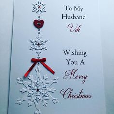 a white christmas card with red ribbon and snowflakes hanging from it's side