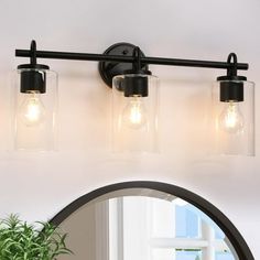 three light bathroom fixture with clear glass shades and black metal frame, on a white wall