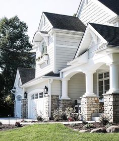 a house with white siding and stone pillars in the front yard, surrounded by trees