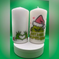 two white candles with the grin face on them and one has a red santa hat