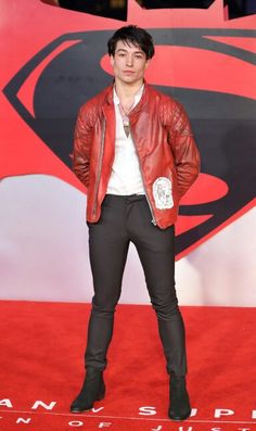 a man in a red leather jacket standing on a red carpet with his hands in his pockets