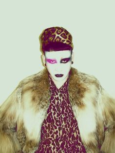 a woman with white makeup and purple eyes is wearing a leopard print fur coat over her dress