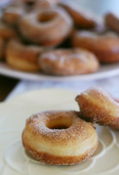 two donuts sitting on top of white plates next to another plate full of doughnuts