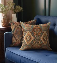 two pillows sitting on top of a blue couch next to a vase with flowers in it