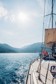 the sun shines brightly on a sailboat in the water with mountains in the background