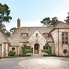 a large brick house surrounded by greenery and stone driveway with an arched doorway leading to the front door