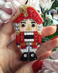 a hand holding a beaded nutcracker ornament with flowers in the background