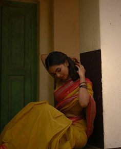 a woman in a yellow sari sitting on the ground with her hands behind her head