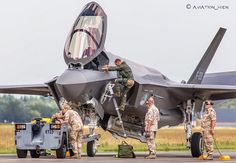 men in fatigues are working on an air force fighter jet that is parked on the tarmac