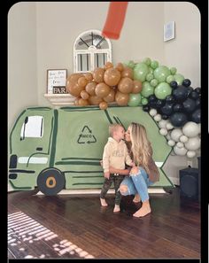 a man and woman kissing in front of a green truck balloon wall with balloons on it