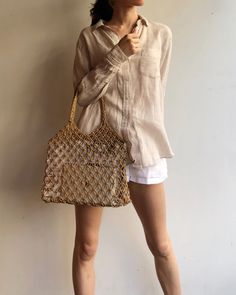 a woman is holding a purse and posing for the camera while leaning against a wall