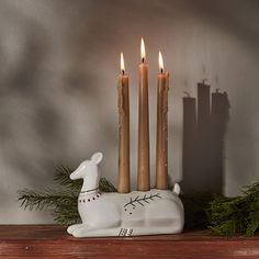 three candles are sitting on top of a mantle with a deer figurine next to it