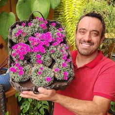 a man holding a basket full of flowers in front of some potted planters