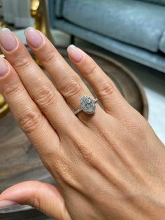 a woman's hand with a diamond ring on top of her left hand, next to a couch