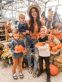 a woman and two children standing in front of pumpkins