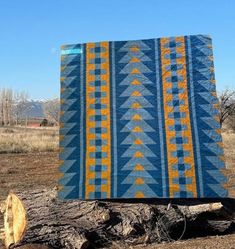 a large blue and yellow quilt sitting on top of a tree stump in the middle of a field