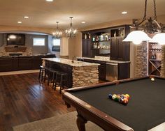 a pool table in the middle of a living room with an entertainment center and bar