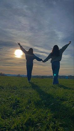 two women holding hands while standing in a field with the sun setting behind them,